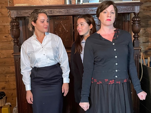 Three women standing in front of fireplace.