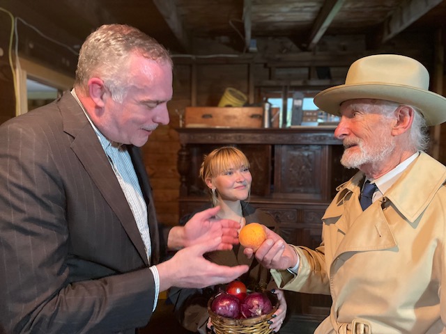 Three people exchanging fruit in rustic setting.