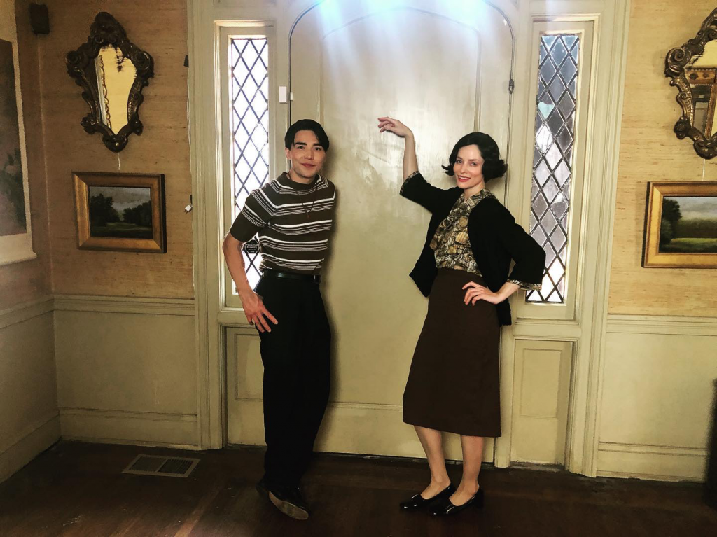 Two people posing in vintage-style hallway.
